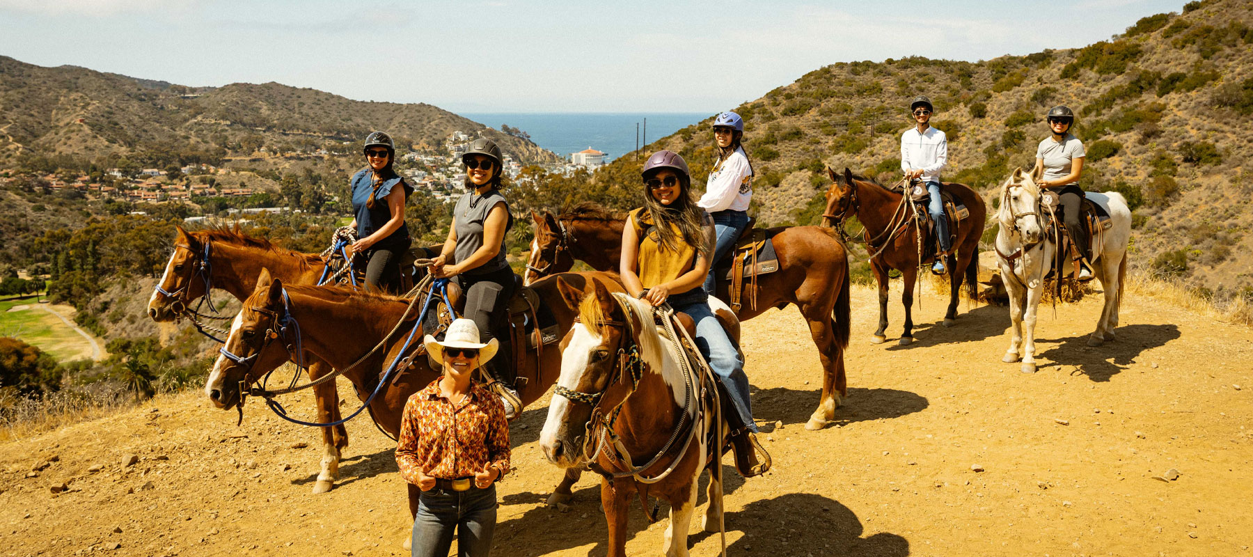 Group of horseback riders on a sunlit trail above the Catalina Island coastline