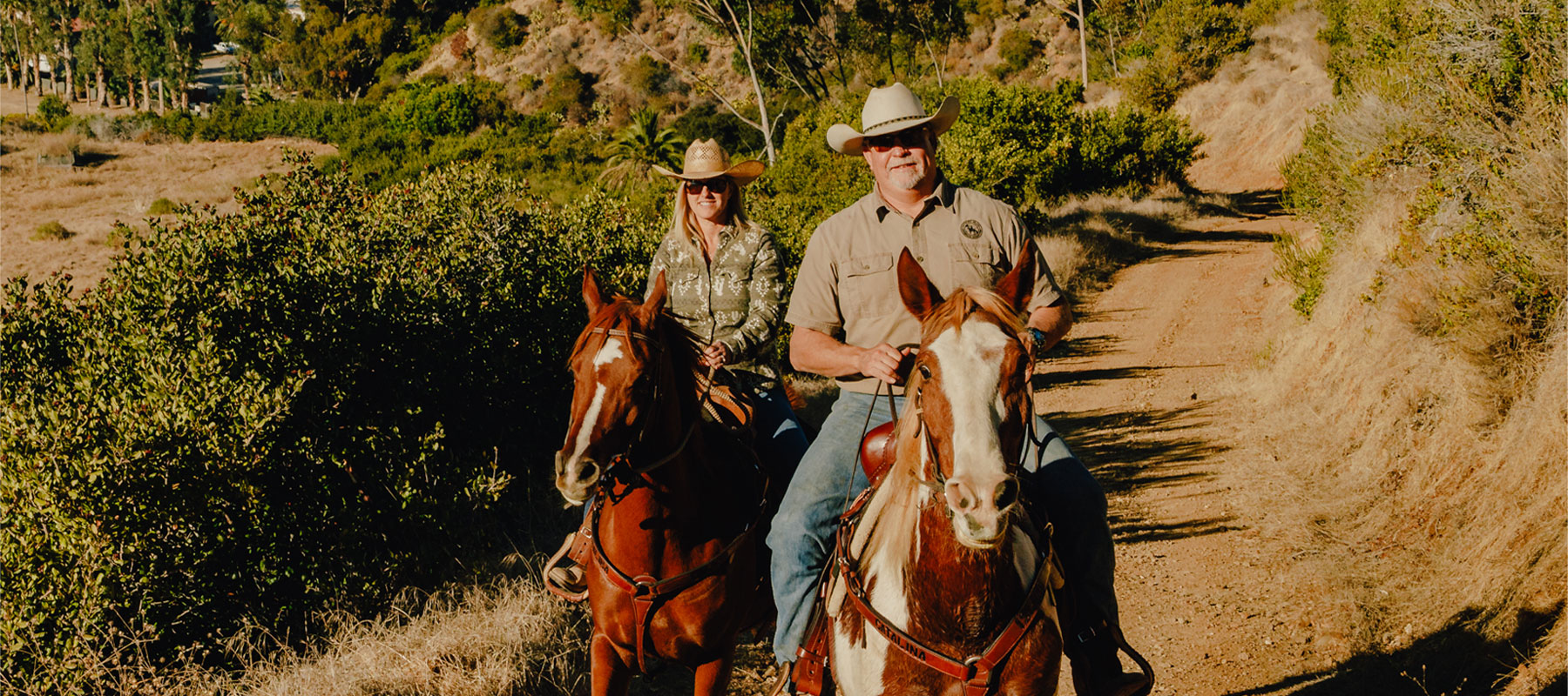Two riders on horseback on a dirt trail through the Catalina Island hills