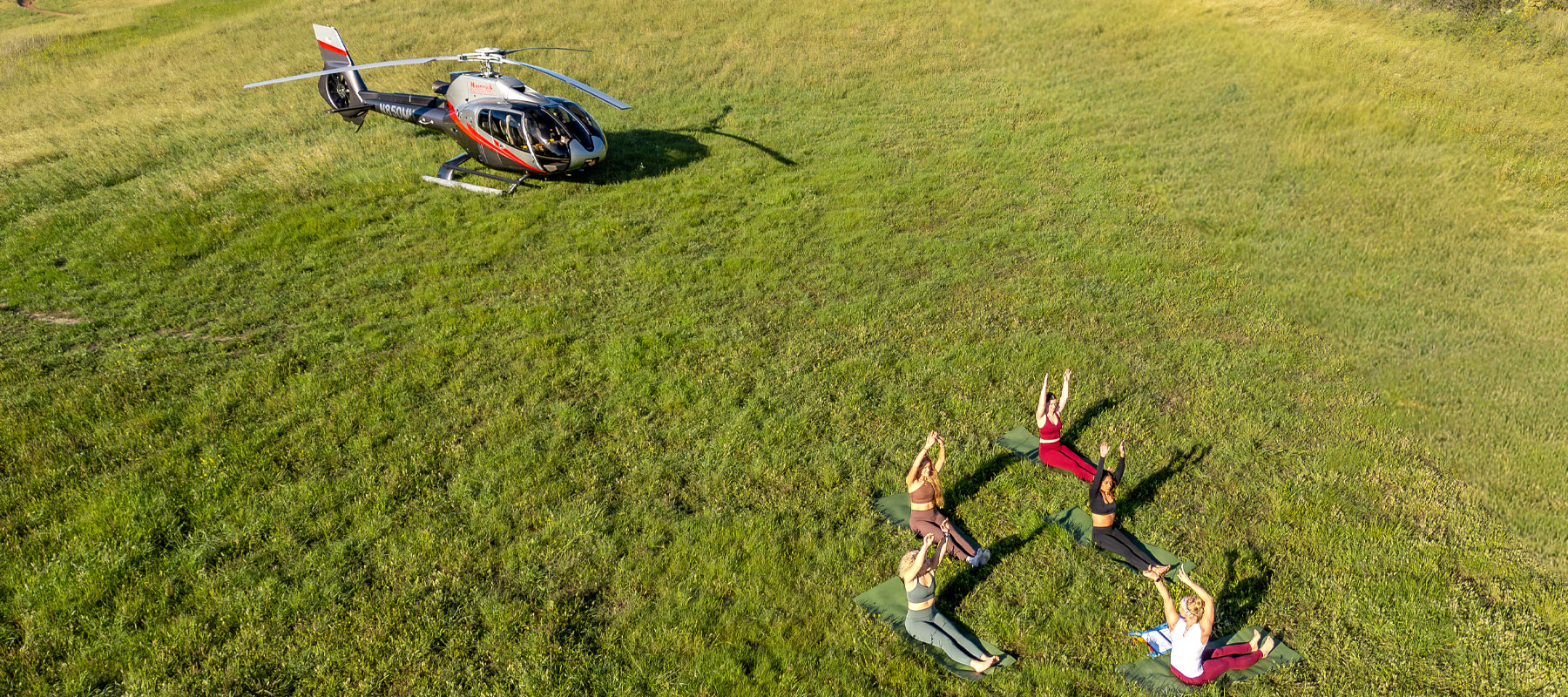 Overhead view of guests doing yoga on the grass near a landed helicopter