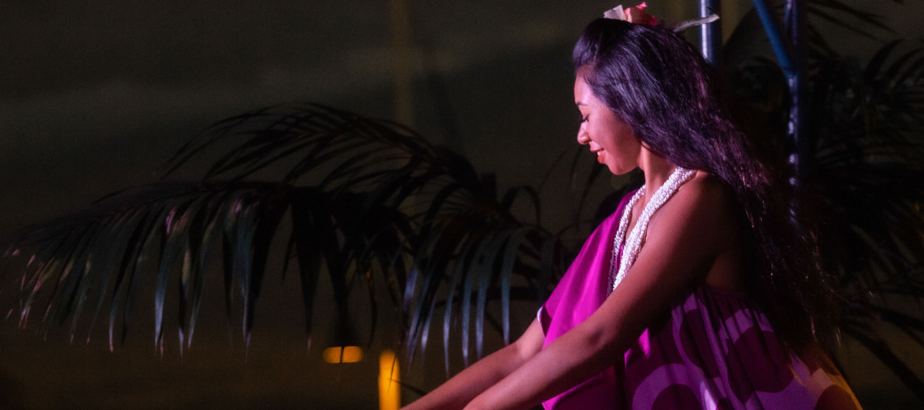 Polynesian dancer in traditional purple attire performing during the luau