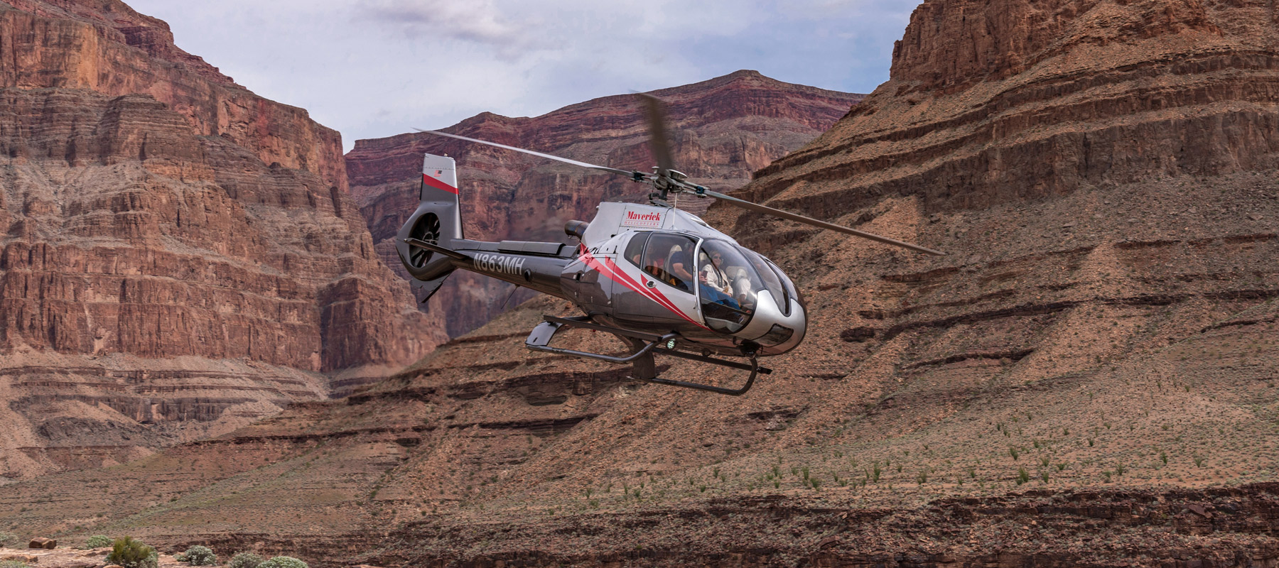 Maverick helicopter flying between the red rock walls of the Grand Canyon